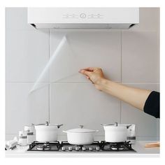 a person is reaching for something on the wall above their stove top burner oven