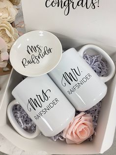 three coffee mugs with their names on them in a box next to some flowers