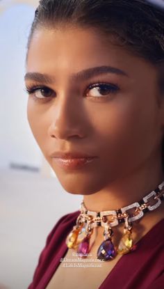 a close up of a woman wearing a necklace and earrings on her neck, looking at the camera