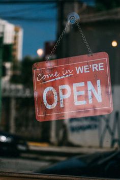 a red sign hanging from the side of a glass door that says come in we're open