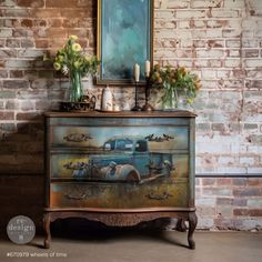 an old dresser has flowers and candles on it in front of a brick wall with a painting