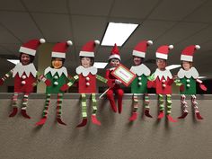 the elfs are lined up in their christmas hats and green pants, with one holding a sign