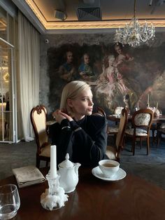 a woman sitting at a table in front of a wall with paintings on the walls