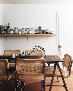 a dining room table and chairs with jars on the shelves above it, in front of an open door