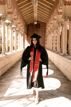 a woman in graduation gown and cap walking down a walkway with columns on both sides