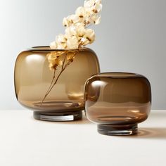 two brown vases with flowers in them on a white tableclothed surface next to each other