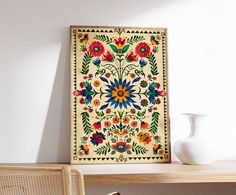 a white vase sitting on top of a wooden table next to a framed art piece