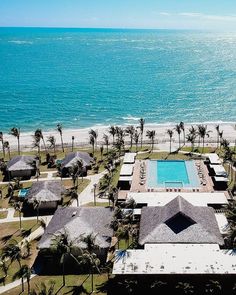 an aerial view of the beach and pool area with thatched roof houses, palm trees, and ocean in the background