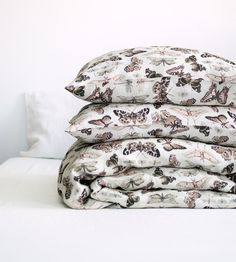 a stack of three pillows sitting on top of a bed covered in butterfly print sheets