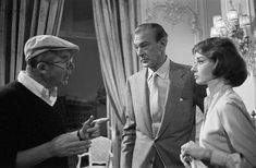 an old photo of two men and a woman talking to each other in a living room