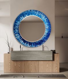 a blue circular mirror hanging on the wall above a wooden vanity with two faucets