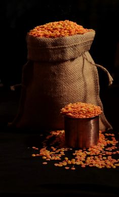 a bag filled with yellow corn kernels on top of a black table next to a metal container