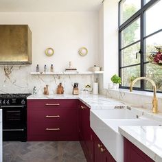 a kitchen with marble counter tops and red cabinets, along with gold accents on the hood