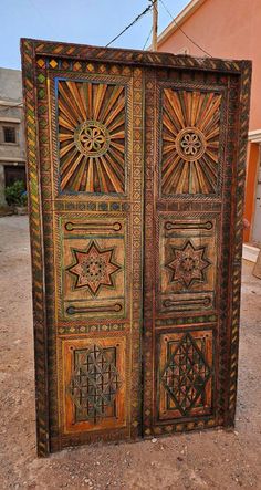 an intricately decorated wooden door in the middle of a dirt area with a building in the background