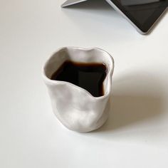 a white cup filled with liquid next to an electronic device on top of a table