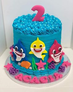 a birthday cake decorated with blue frosting and fondant decorations, featuring shark characters