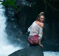 a woman sitting on top of a rock next to a waterfall