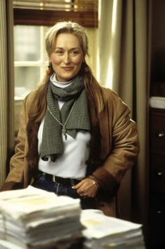 a woman is standing in front of stacks of papers and wearing a scarf around her neck