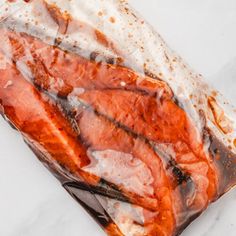 a piece of meat wrapped in plastic on top of white paper with brown and black spots