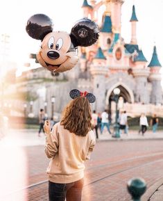 a woman holding onto mickey mouse balloons in front of a castle