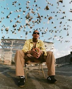 a man sitting in a chair with birds flying around him and his feet on the ground