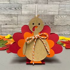 a paper turkey with a bow on it's head sitting in front of some fall leaves