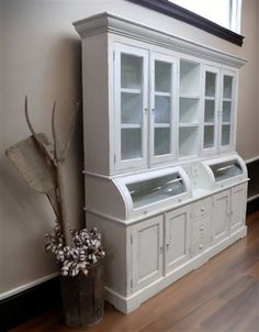 a white china cabinet sitting next to a vase with flowers in it on top of a hard wood floor