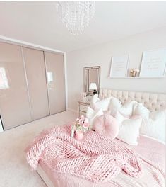 a bed with pink blankets and pillows in a bedroom next to a chandelier