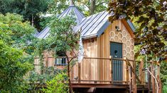 a small wooden cabin in the woods surrounded by trees and bushes, with a deck leading up to it