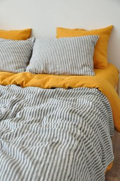 an unmade bed with yellow pillows and striped comforter on the bottom, next to a white headboard