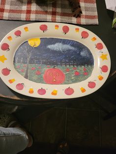 a plate with an image of a pumpkin and apples painted on the front is sitting on a table