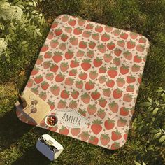 an apple and strawberry print picnic blanket on the grass