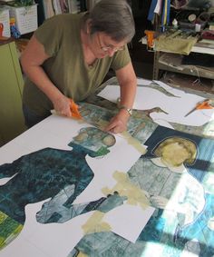 a woman is cutting out pictures on a large sheet of paper with scissors and glue