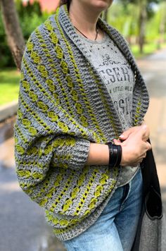 a woman wearing a gray and yellow crochet shawl standing on the street