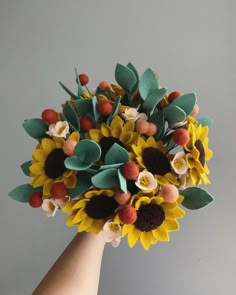 a hand holding a bouquet of sunflowers with leaves and flowers on it's head