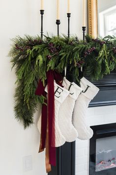 stockings hanging from a mantle with evergreen and pine cones on it, along with candles