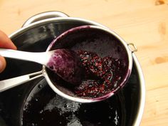 a person is holding a spoon over a pot full of blueberry sauce on a wooden table