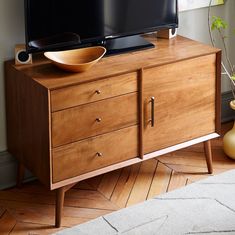 a wooden cabinet with two televisions on top of it and a vase next to it