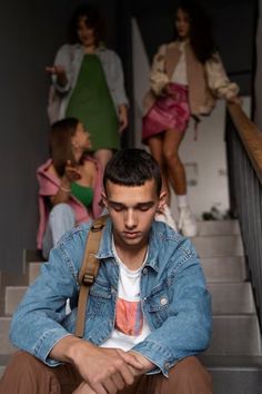 a young man sitting on the stairs in front of other models wearing clothes and jeans