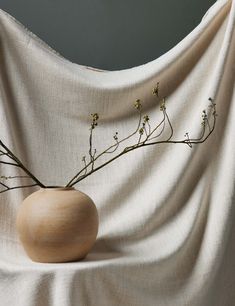 a vase with some flowers in it sitting on a cloth covered tablecloth draped by a drape