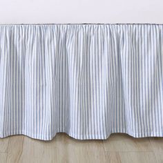 a blue and white striped bed skirt on a wooden floor with a wall in the background