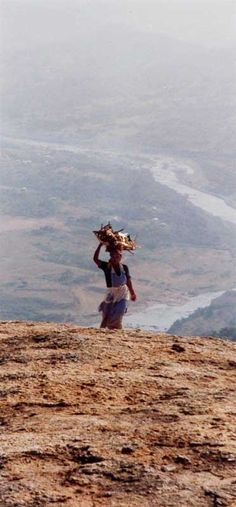 a person standing on top of a hill with a hat over their head and a river in the background