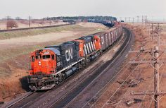 an orange and black train traveling down tracks next to dry grass, power lines and telephone poles