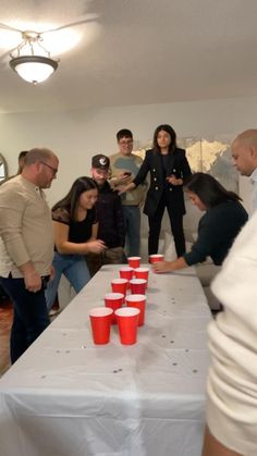 a group of people standing around a table with red cups on it and one man in the middle