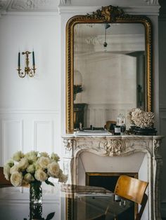 a room with a fireplace, mirror and flowers on the table in front of it