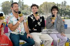 three men sitting on a bench with microphones in front of them and one man holding a