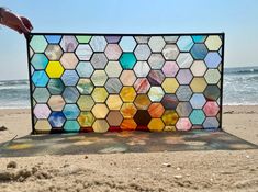 a person is holding up a stained glass piece on the beach with water in the background