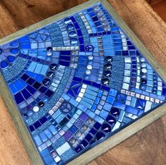 a close up of a blue mosaic tile on a wooden table with a wood frame