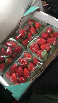 the box is full of strawberries in plastic wrap and sitting on someone's lap