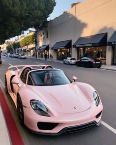 two pink sports cars are parked on the side of the road in front of shops